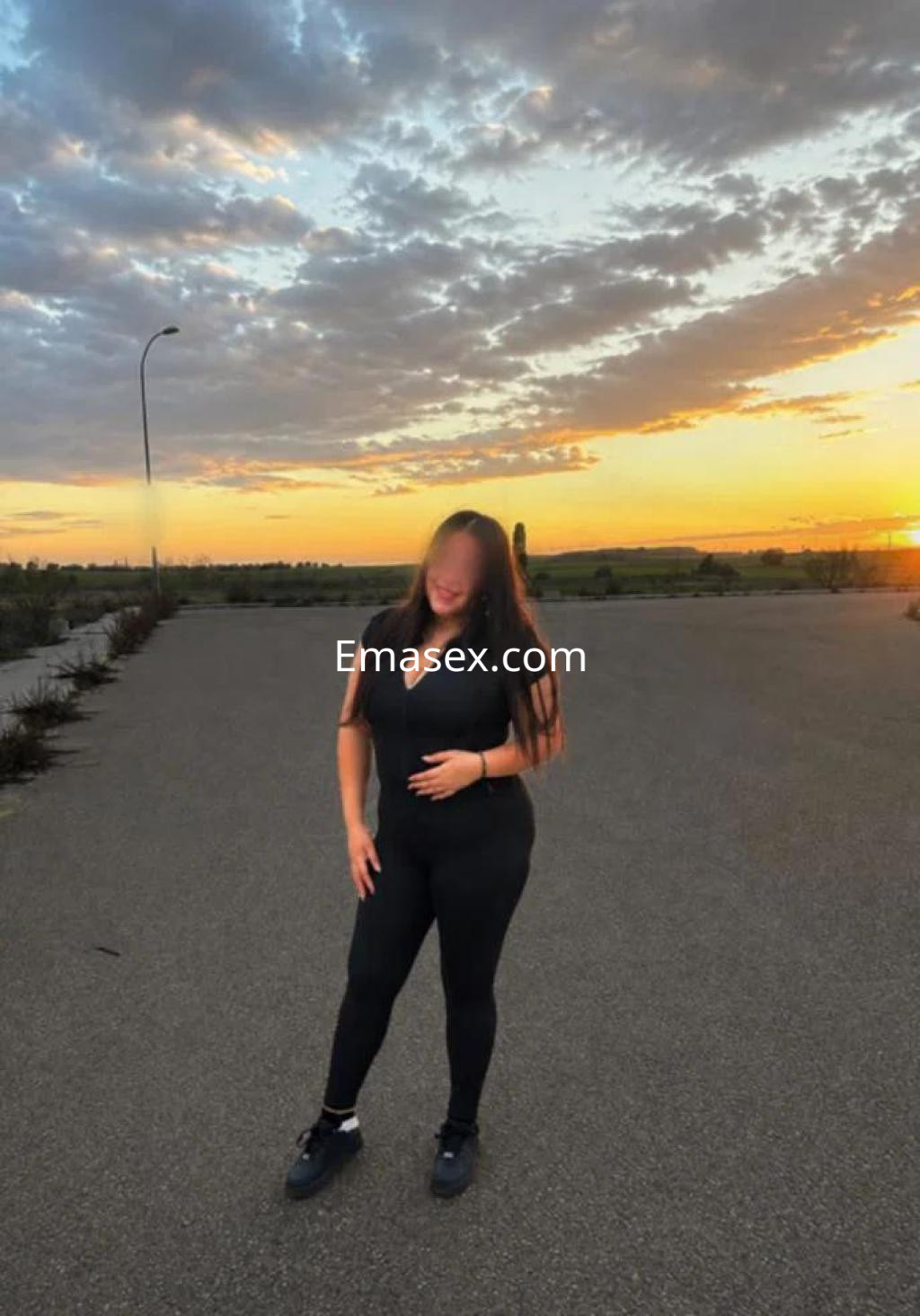 Puta de cabello largo y lacio, vestida con un atuendo negro, posando al atardecer en una zona despejada de Valladolid.