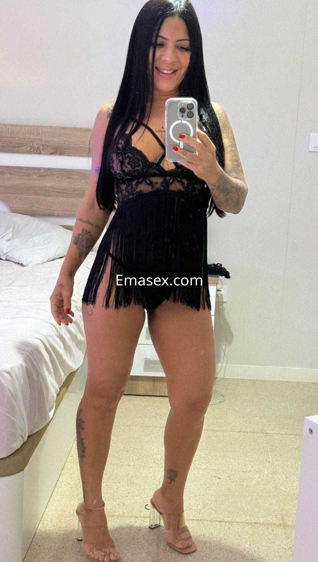 Escort en Sevilla posando en un espejo, con un conjunto de lencería negra y sandalias transparentes.