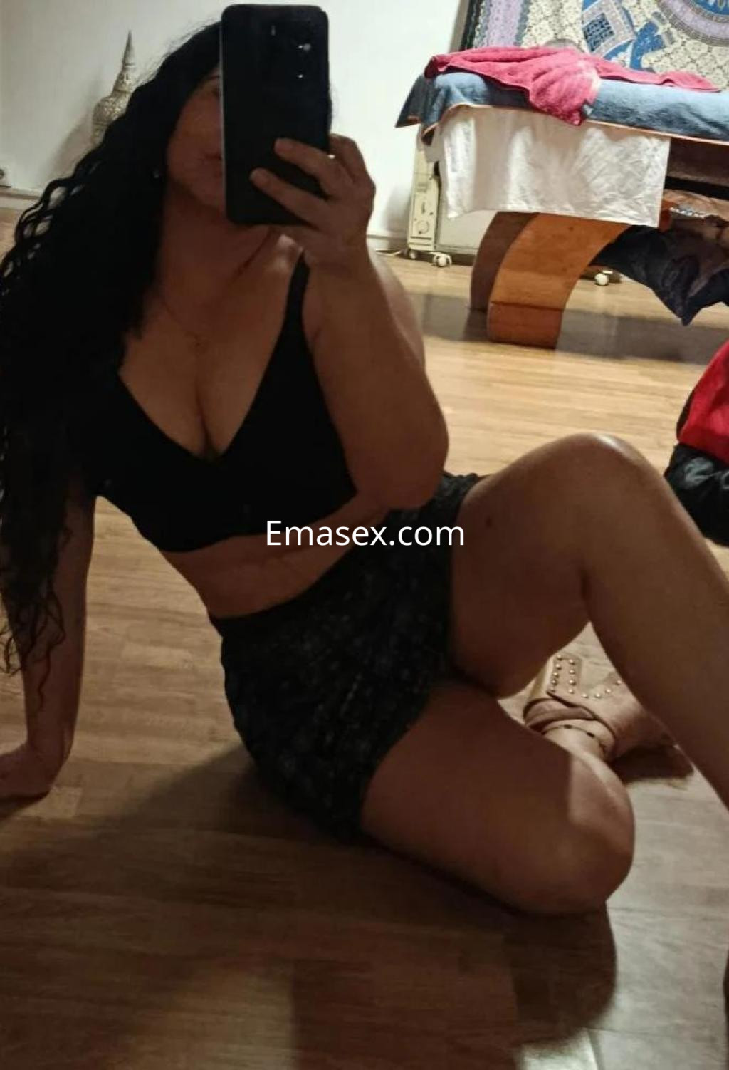 Puta con cabello largo y rizado, luciendo un top negro y una falda corta, en un ambiente acogedor de Sevilla.