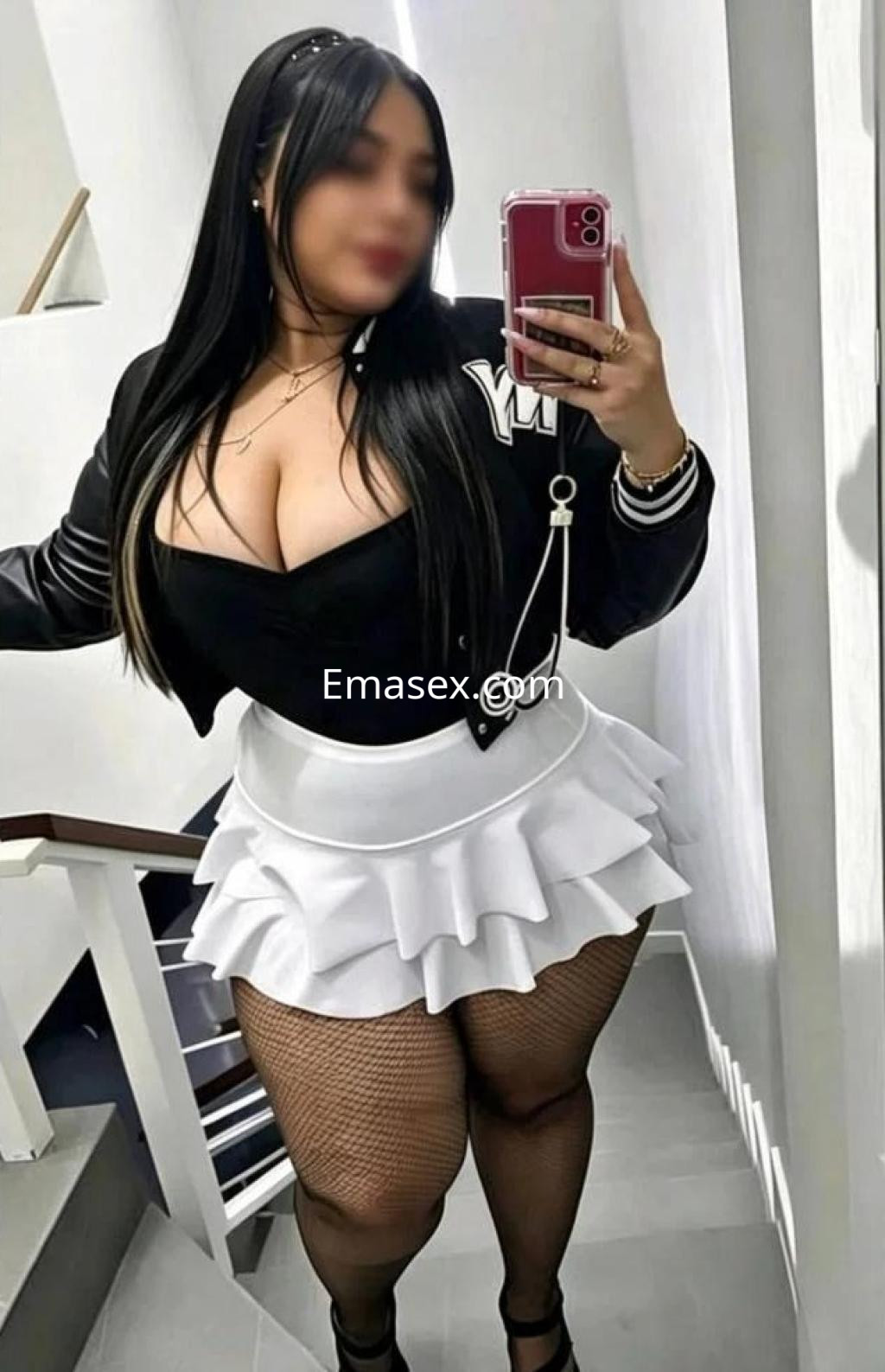 Puta en Málaga con cabello largo y lacio, vestida con blusa negra y falda blanca, posando en una escalera.