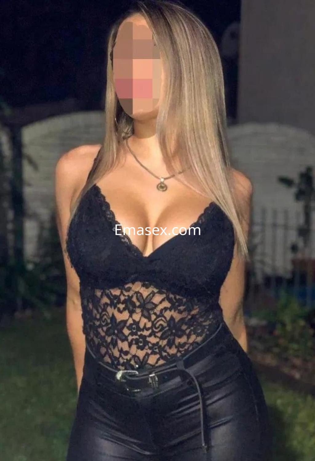 Escort en Cádiz, con cabello rubio y lacio, viste un body negro de encaje y pantalones ajustados, posando en un entorno exterior.