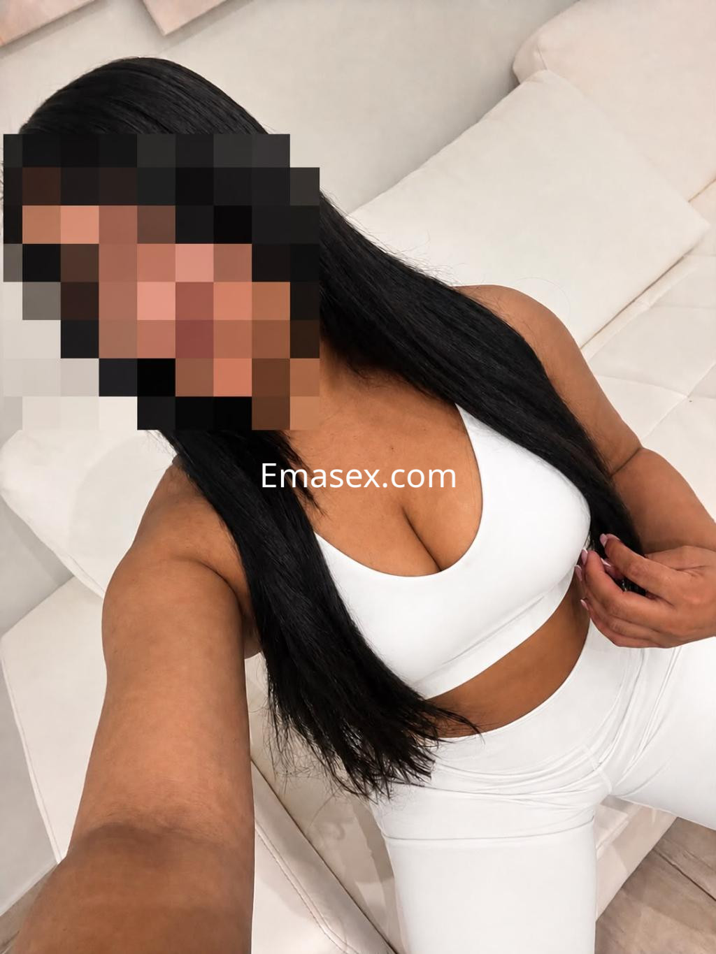 Escort en Córdoba viste un conjunto deportivo blanco que resalta su figura, posando en un sofá claro.