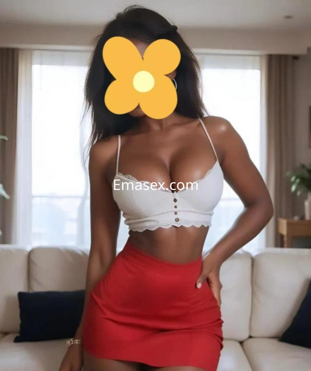 Puta de piel morena, viste un top blanco y una falda roja ceñida, posando en un salón iluminado en Alicante.