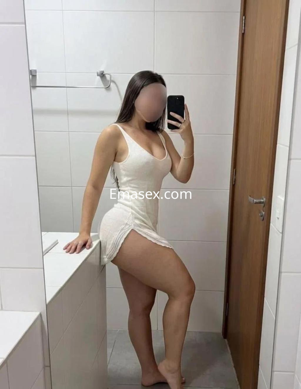Escort en Lugo posando en un baño con un vestido blanco ajustado, mostrando confianza y elegancia.