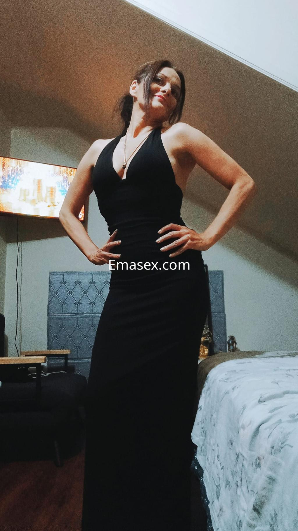 Escort en Vigo vistiendo un vestido negro largo con escote profundo, posando con confianza en un ambiente interior.