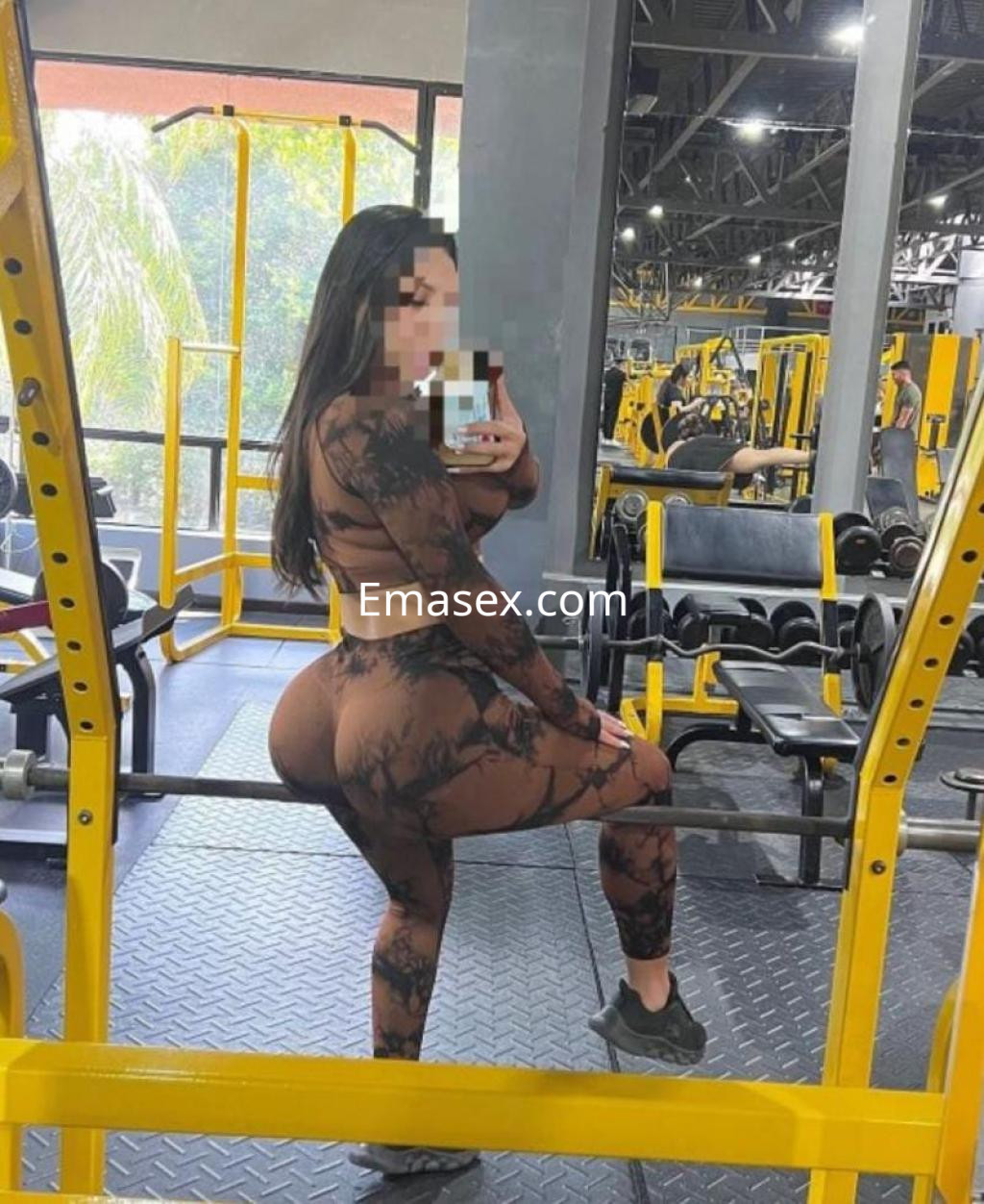 Escort en Bilbao posando en un gimnasio, vistiendo un conjunto deportivo de mallas y top ajustado.