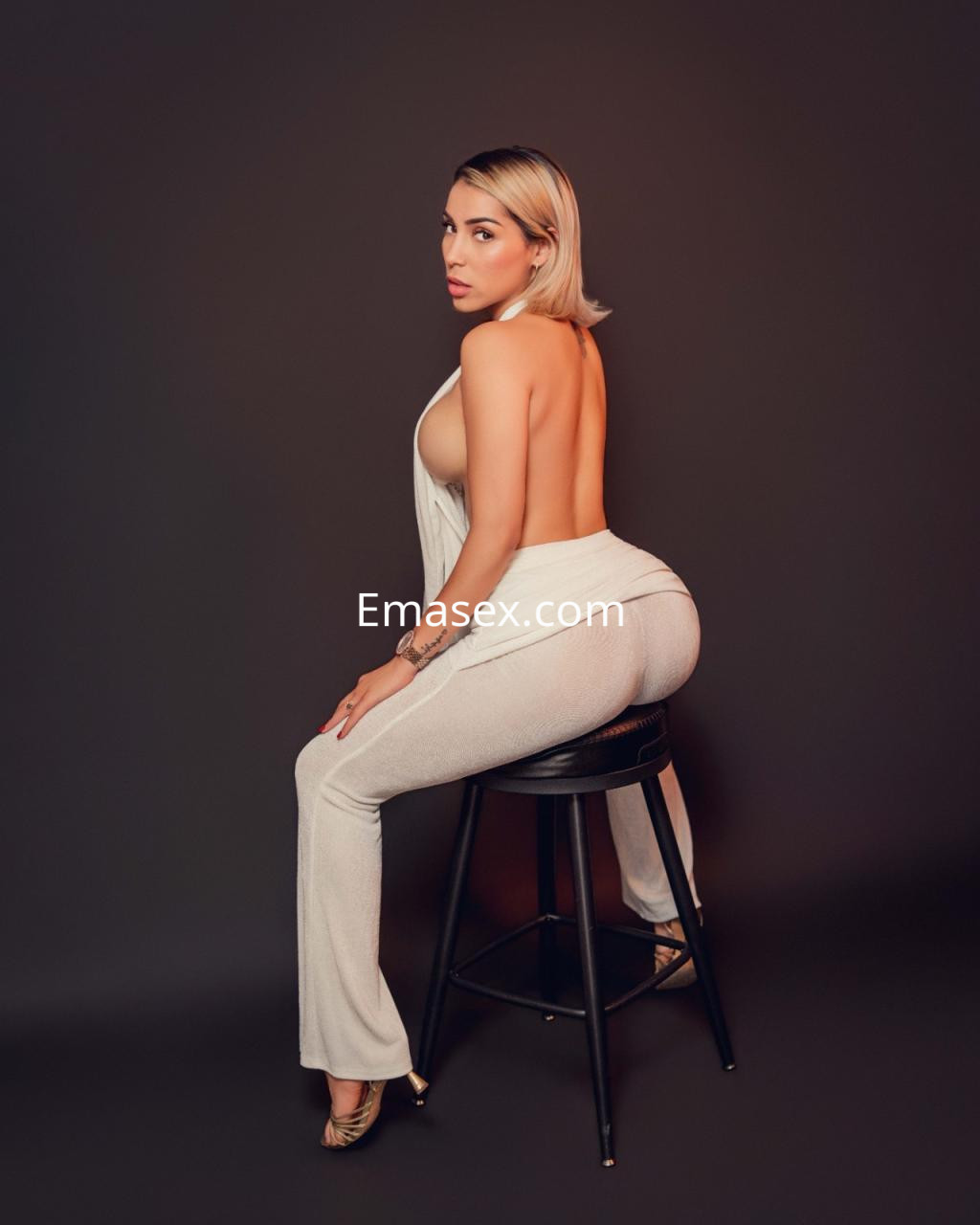 Puta posando de espaldas en una silla, con un conjunto blanco que resalta su figura en Santander.