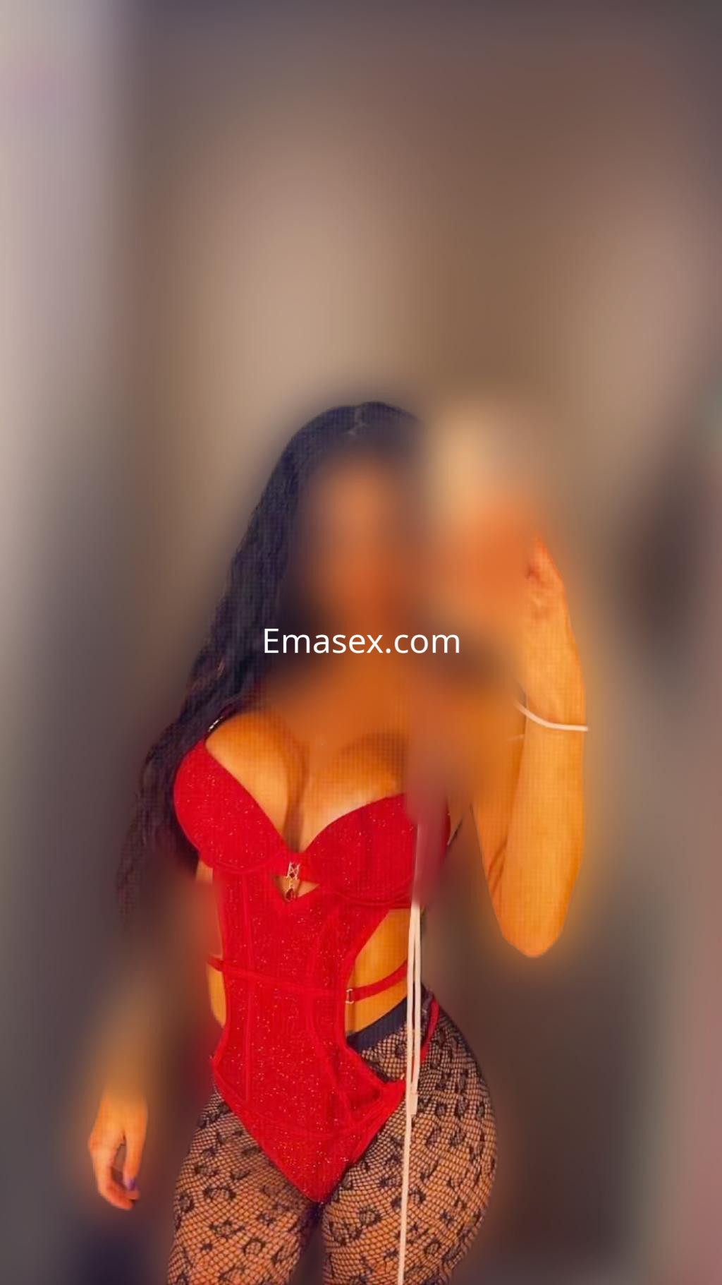 Escort en Oviedo con cabello oscuro y ondulado, luciendo un corsé rojo y mallas negras en un ambiente desenfocado.