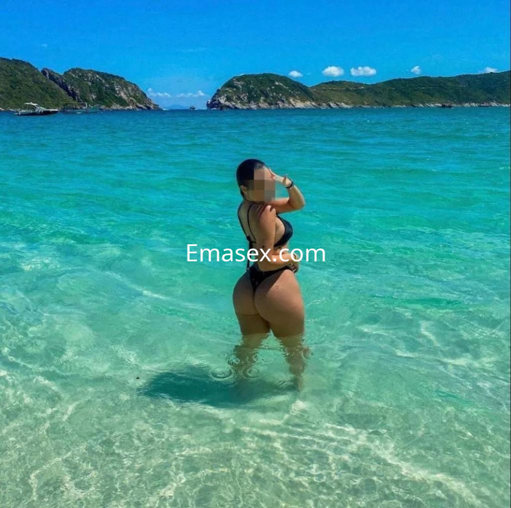 Puta de pie en aguas cristalinas de Almería, luciendo un bikini negro y mostrando una pose coqueta.