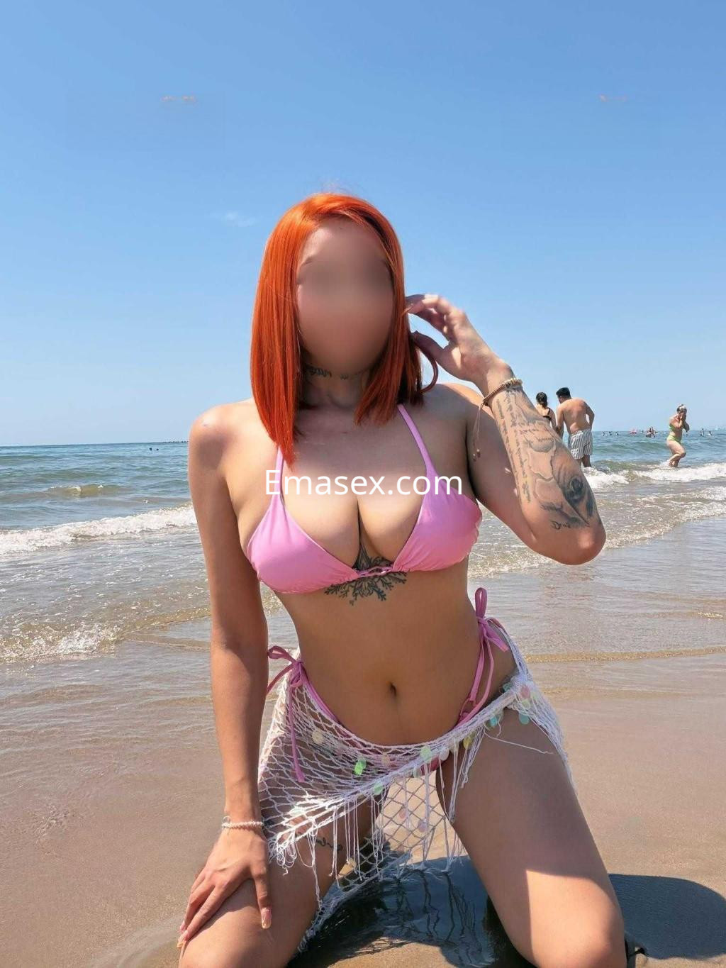 Puta con pelo corto naranja, posando en la playa con bikini rosa y pareo de red, en Almería.