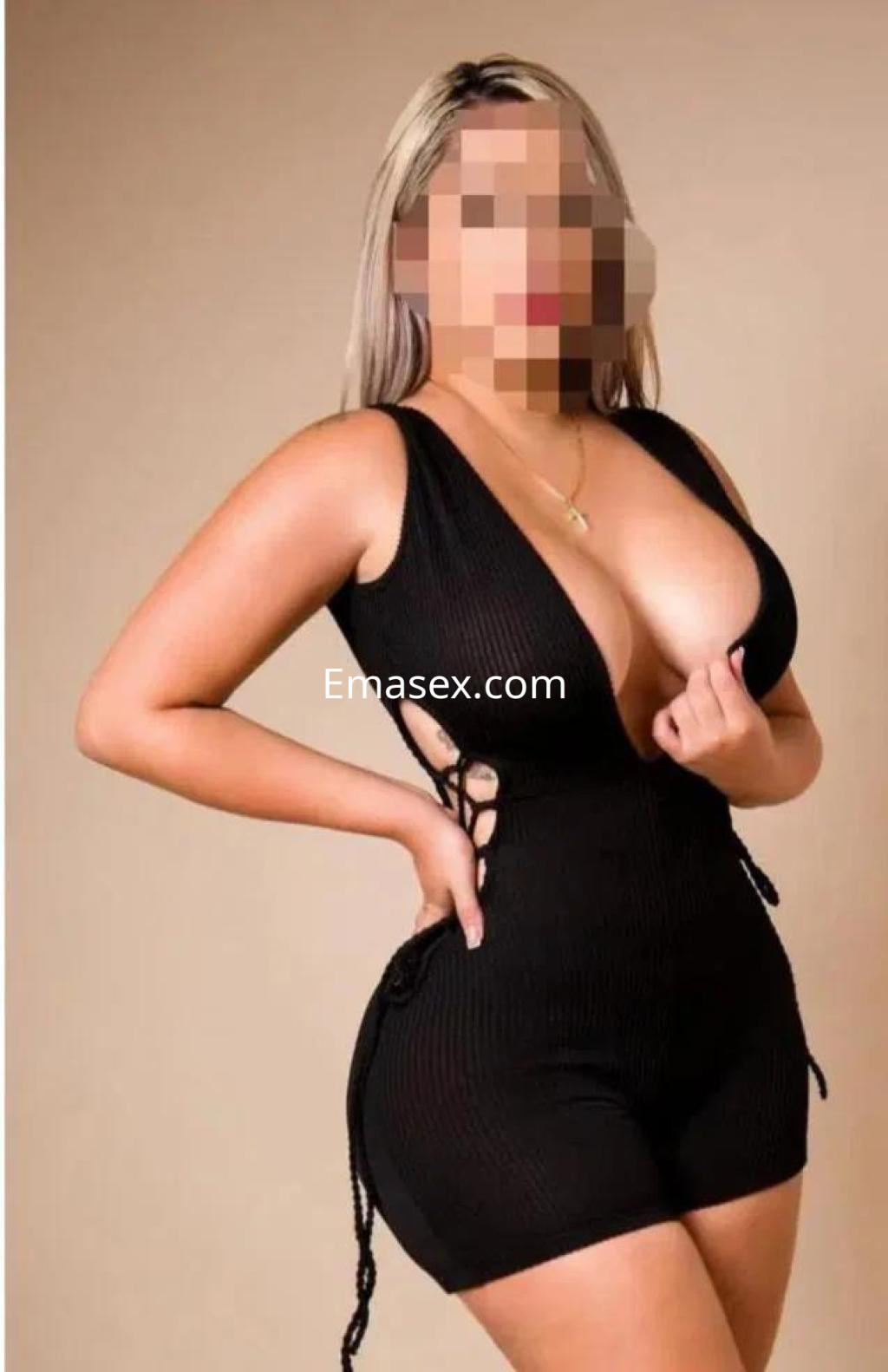 Escort en Badajoz con cabello rubio, luciendo un vestido negro ajustado y posando de lado con una expresión coqueta.