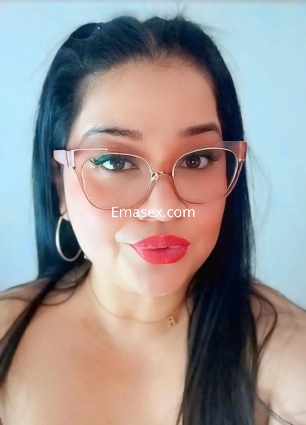 Puta con cabello largo y lacio, maquillaje destacado y gafas, posando frente a fondo claro en Granada.