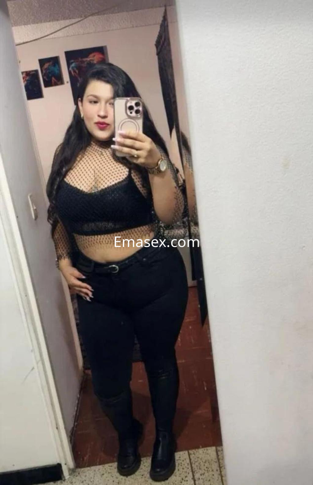 Puta de Lleida posando frente al espejo con top de red negra y pantalones ajustados, luciendo un maquillaje llamativo.
