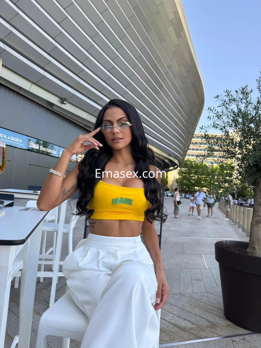 La puta viste un top amarillo y pantalones blancos, posando con gafas en un ambiente urbano de Oviedo.