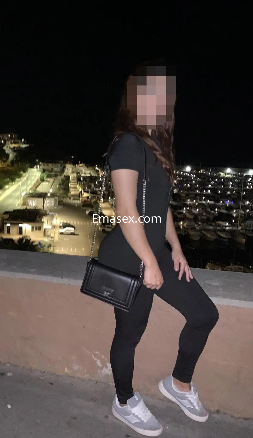 La puta viste un ajustado conjunto negro y zapatillas blancas, posando de noche frente a un puerto en Zaragoza.