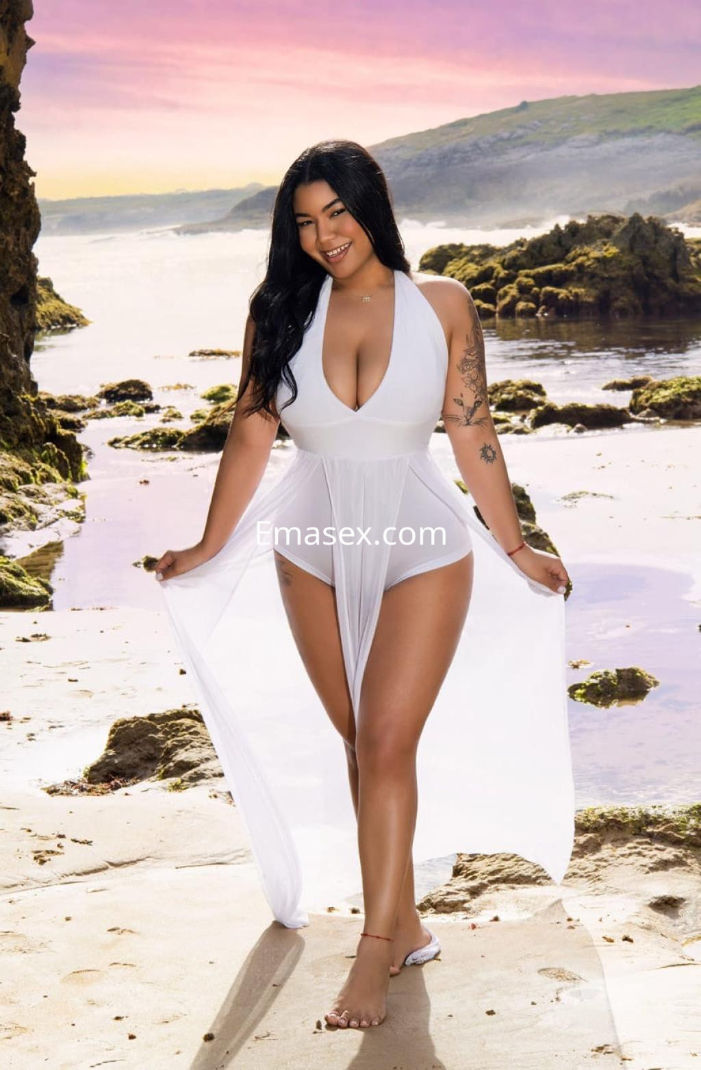 Escort en Pamplona con cabello largo y oscuro, vestida con un traje de baño blanco, posando en la playa.