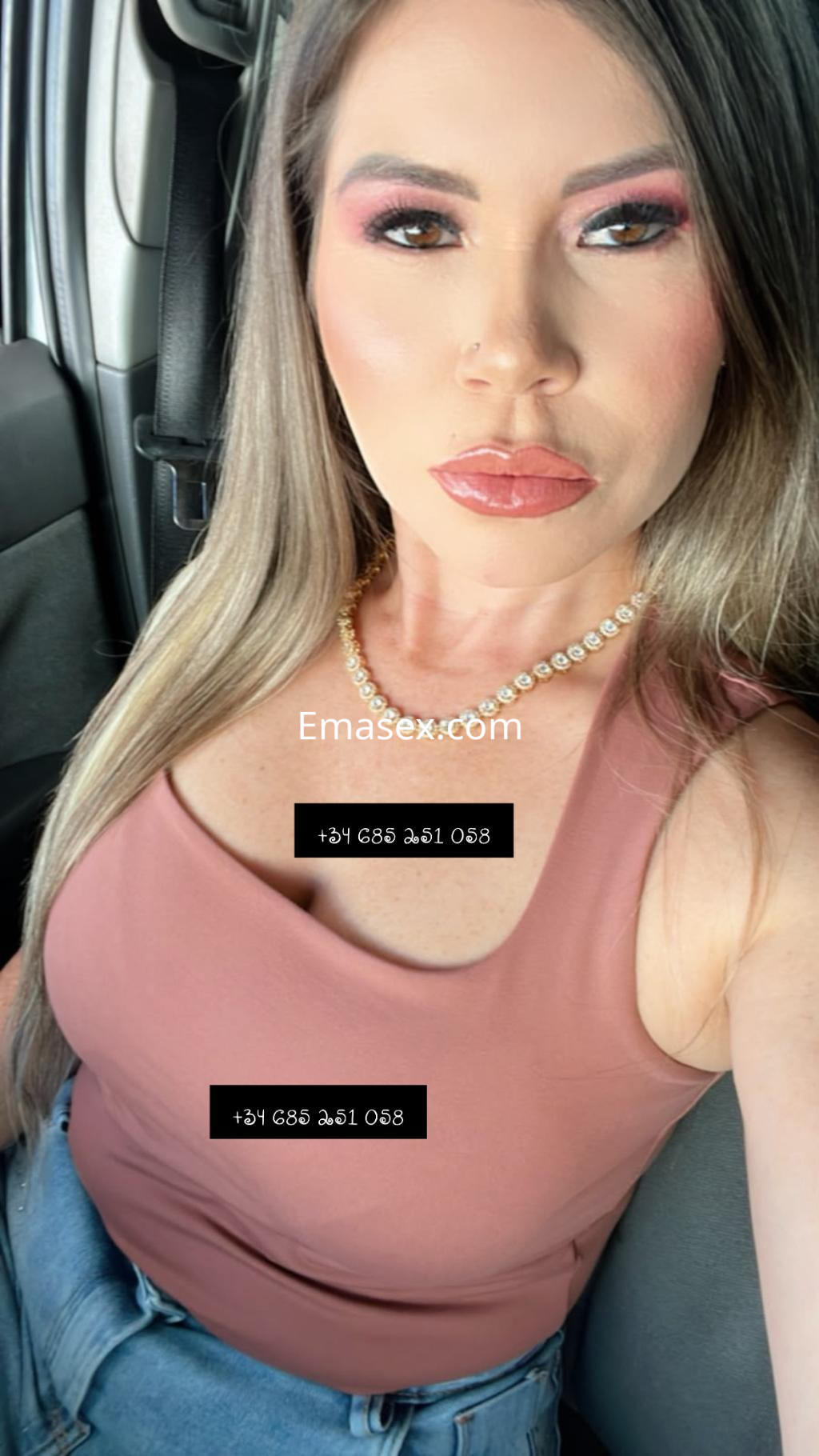 La escort en Vigo luce un top ajustado de color rosa y jeans, con un maquillaje destacado y cabello largo.