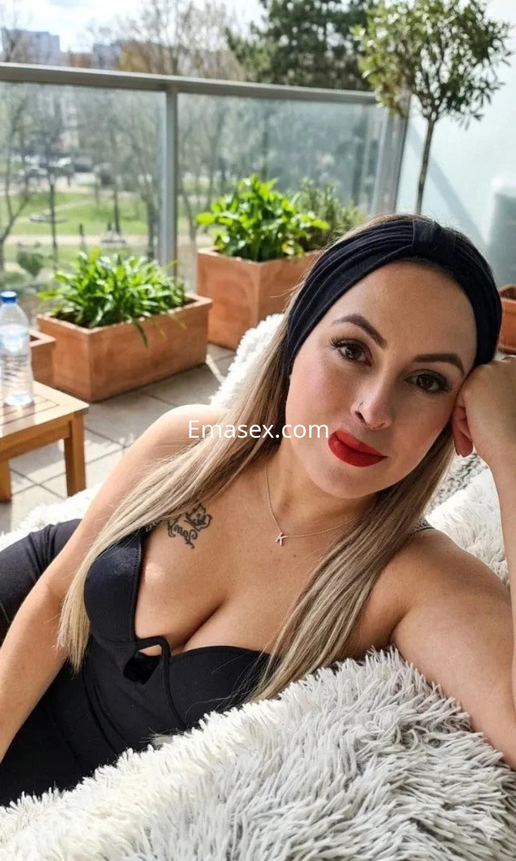 La puta posando en un balcón, lleva un vestido negro, tiene el cabello rubio y labios pintados de rojo.