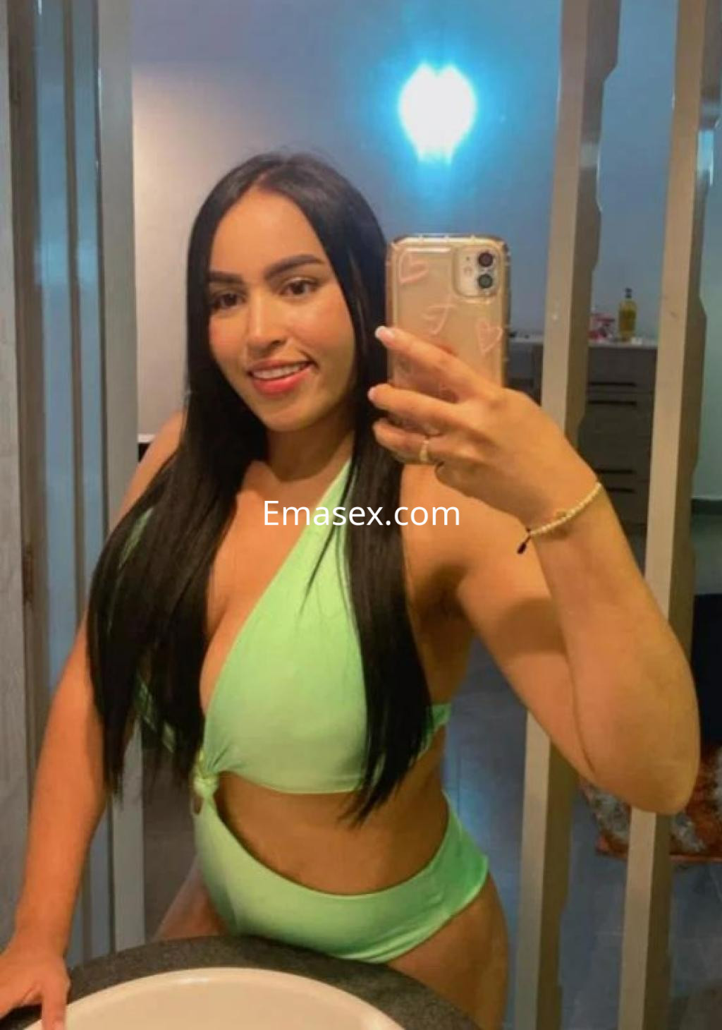 Escort en Madrid con cabello largo y lacio, vestida con un bañador verde mientras sonríe frente al espejo.