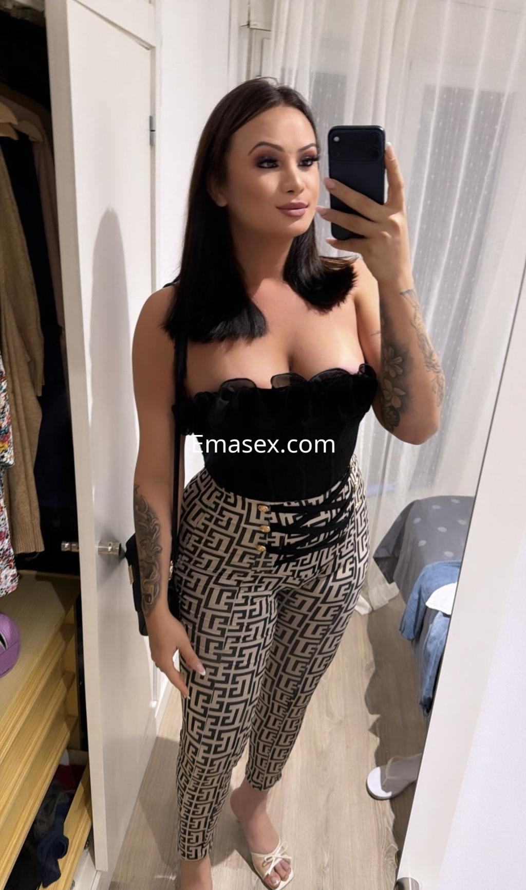 Escort trans en Oviedo posando con un top negro sin mangas y pantalones ajustados con diseño gráfico.