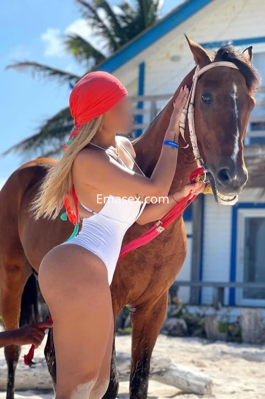 La puta posando en la playa de Santander, viste un traje de baño blanco y lleva un pañuelo rojo en la cabeza.