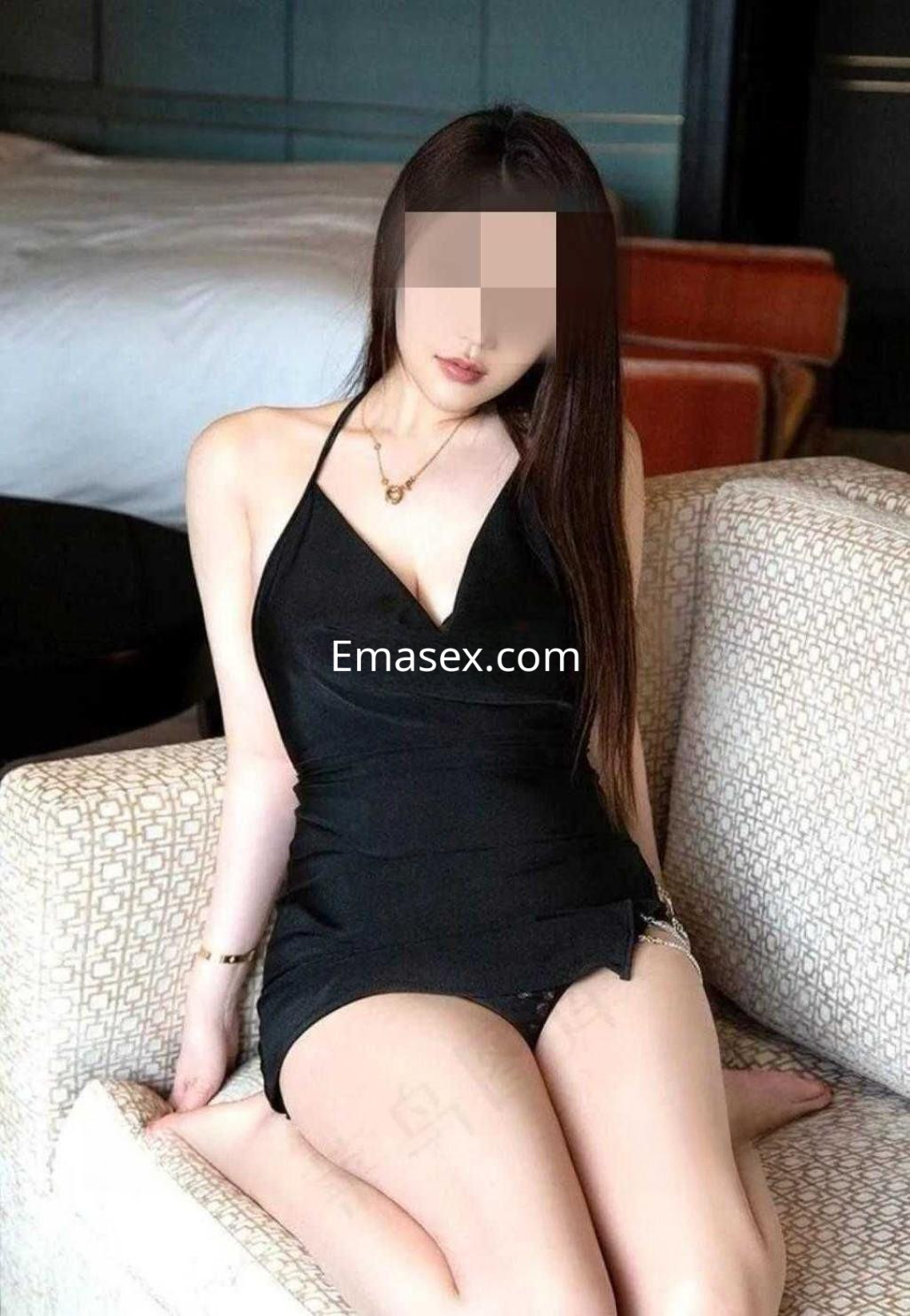 Escort en Alicante sentada en un sofá, vistiendo un vestido negro ajustado y con cabello largo y lacio.