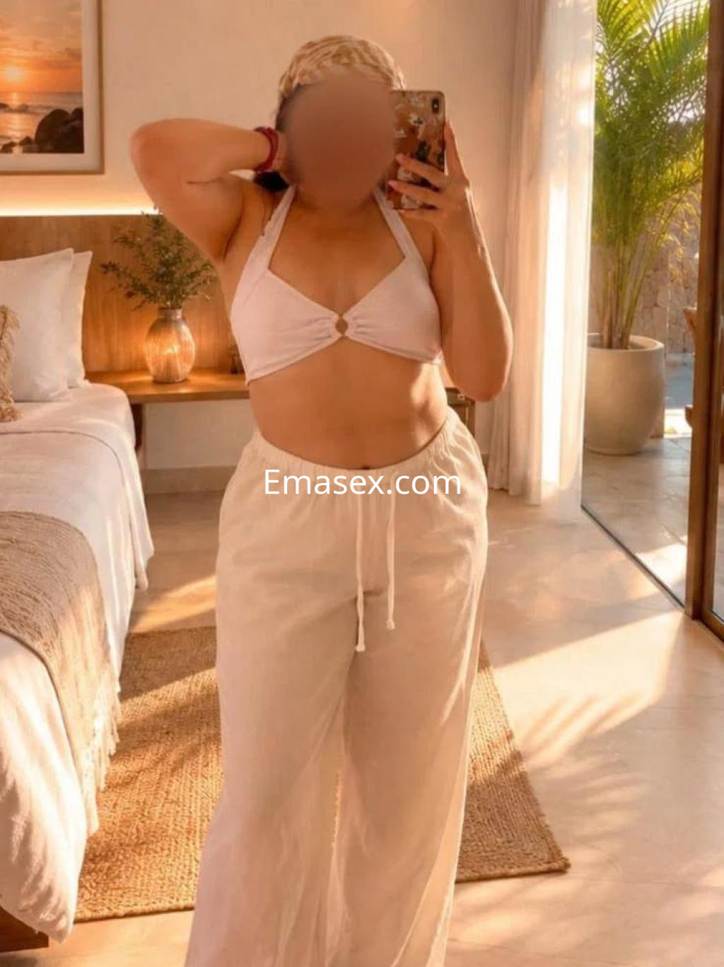 Escort en Almería con top blanco y pantalones claros, posando en un ambiente luminoso y acogedor.