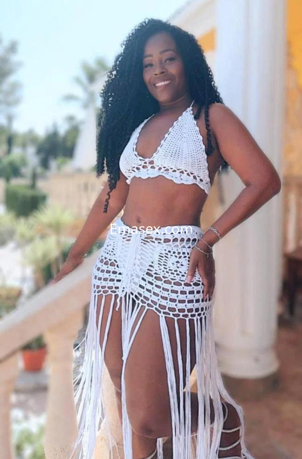 Escort en Almería con cabello rizado, vistiendo un conjunto de crochet blanco que revela su figura.