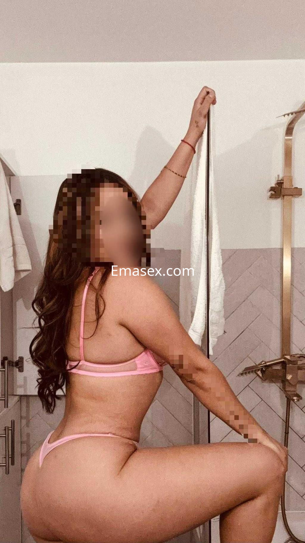 Escort en Badajoz posando de lado con lencería rosa, en un ambiente de baño con azulejos claros.