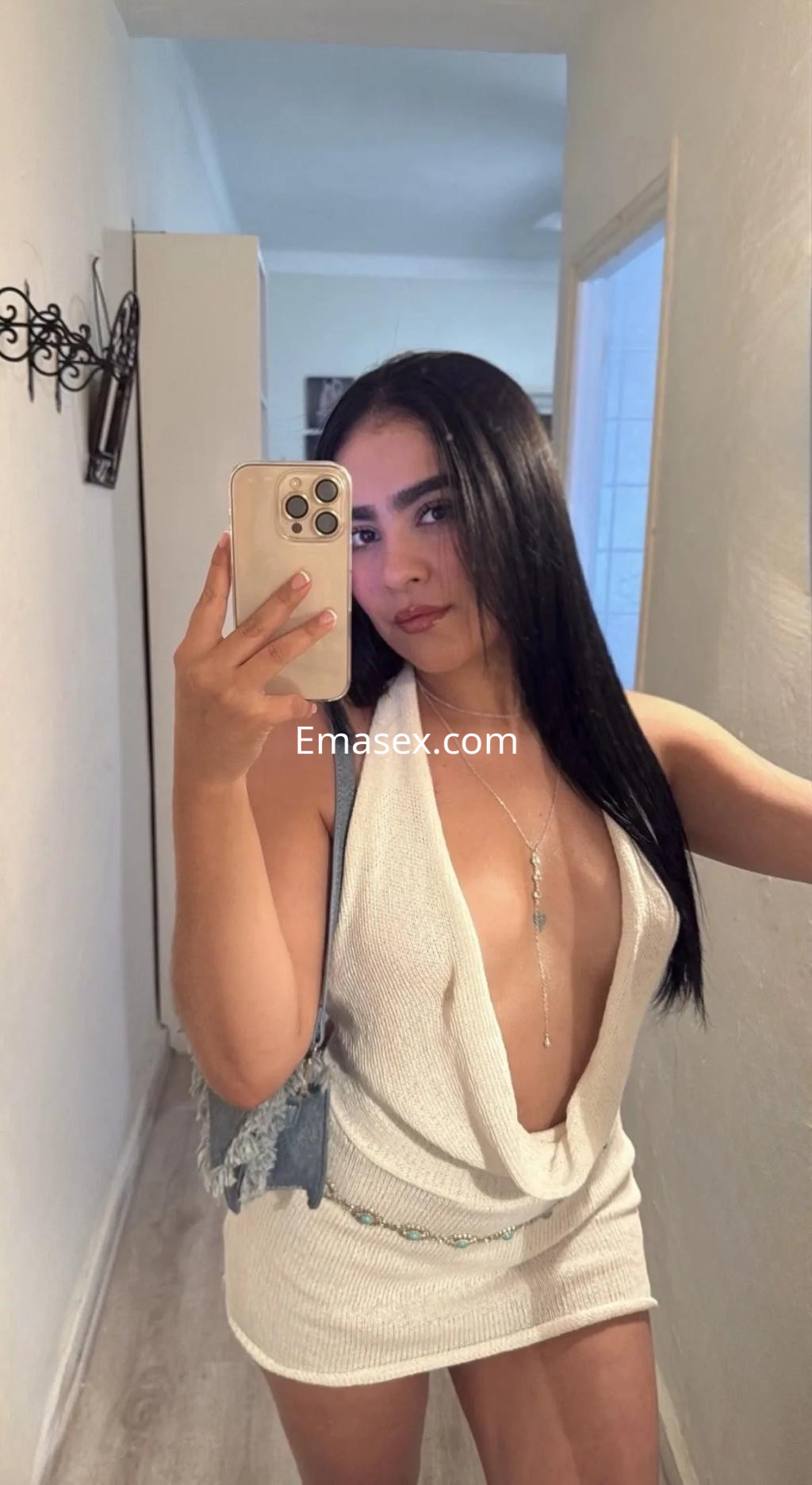 Escort en Palma de Mallorca luciendo un vestido blanco de escote profundo y cabello largo y lacio mientras se toma una selfie.