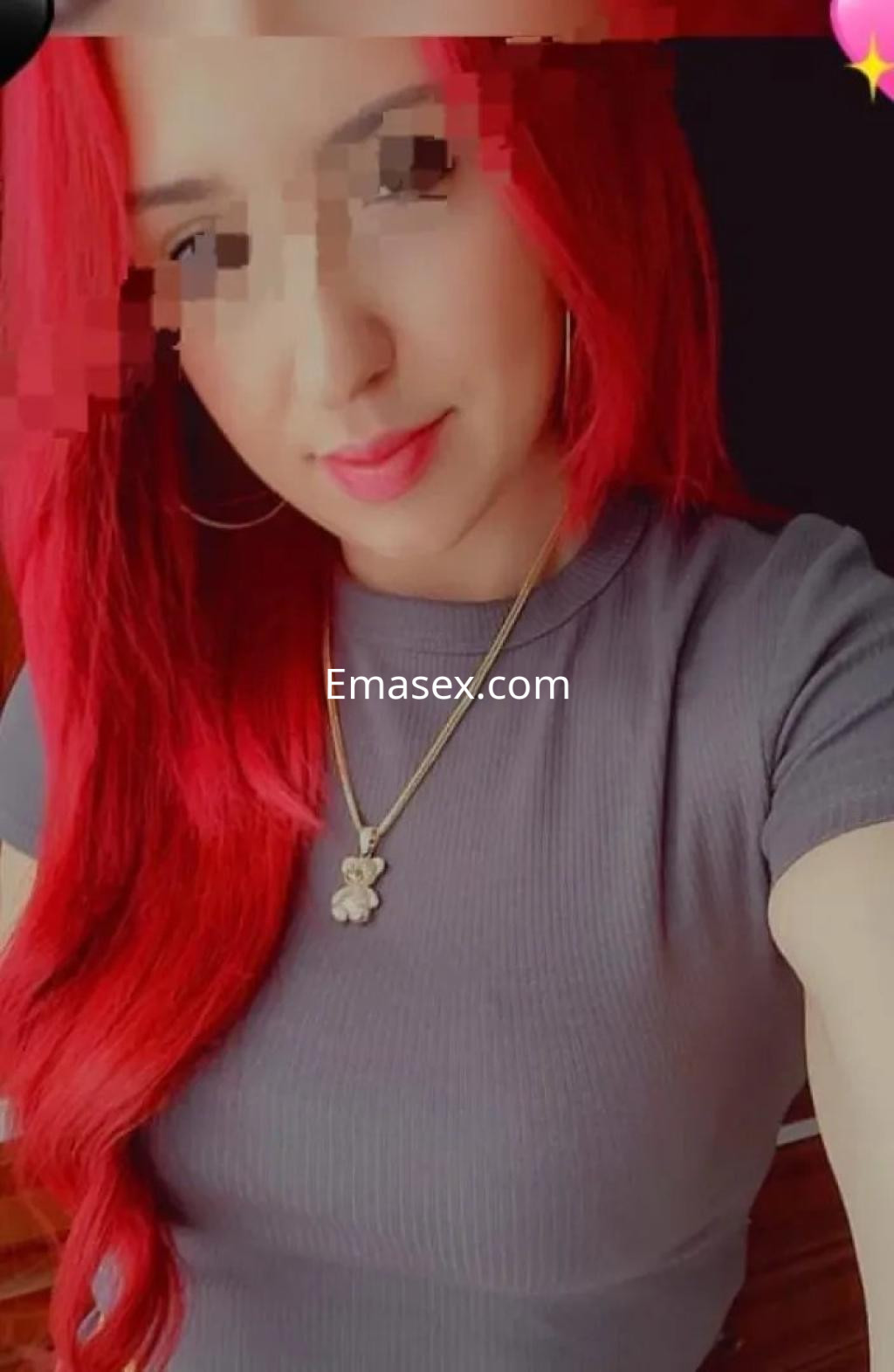 Escort en Coruña con cabello largo y rojo, vistiendo una blusa gris ajustada y con pendientes grandes.