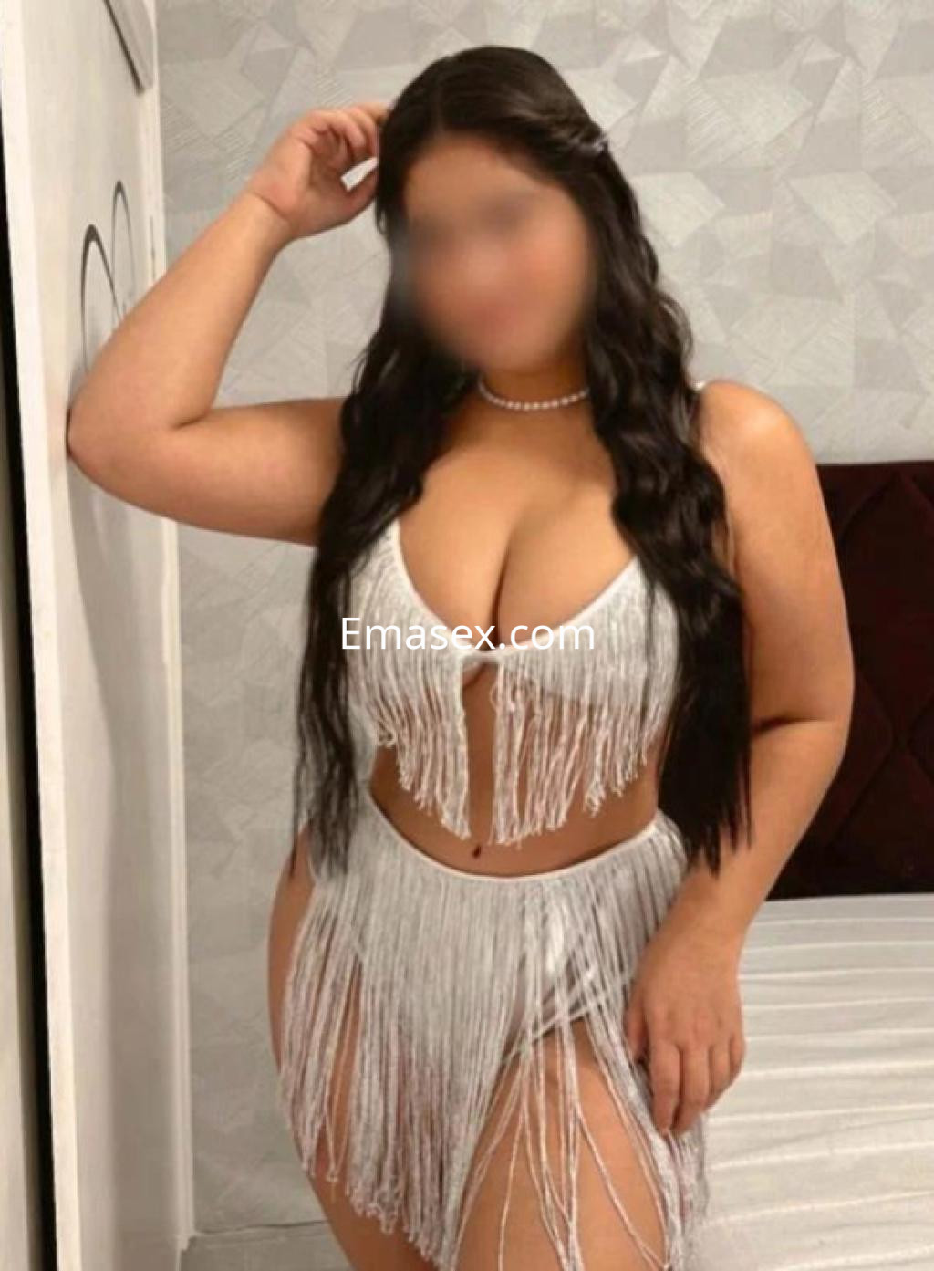Puta en Tenerife luce un conjunto blanco con flecos, posando con una mano en la cabeza y una mirada seductora.