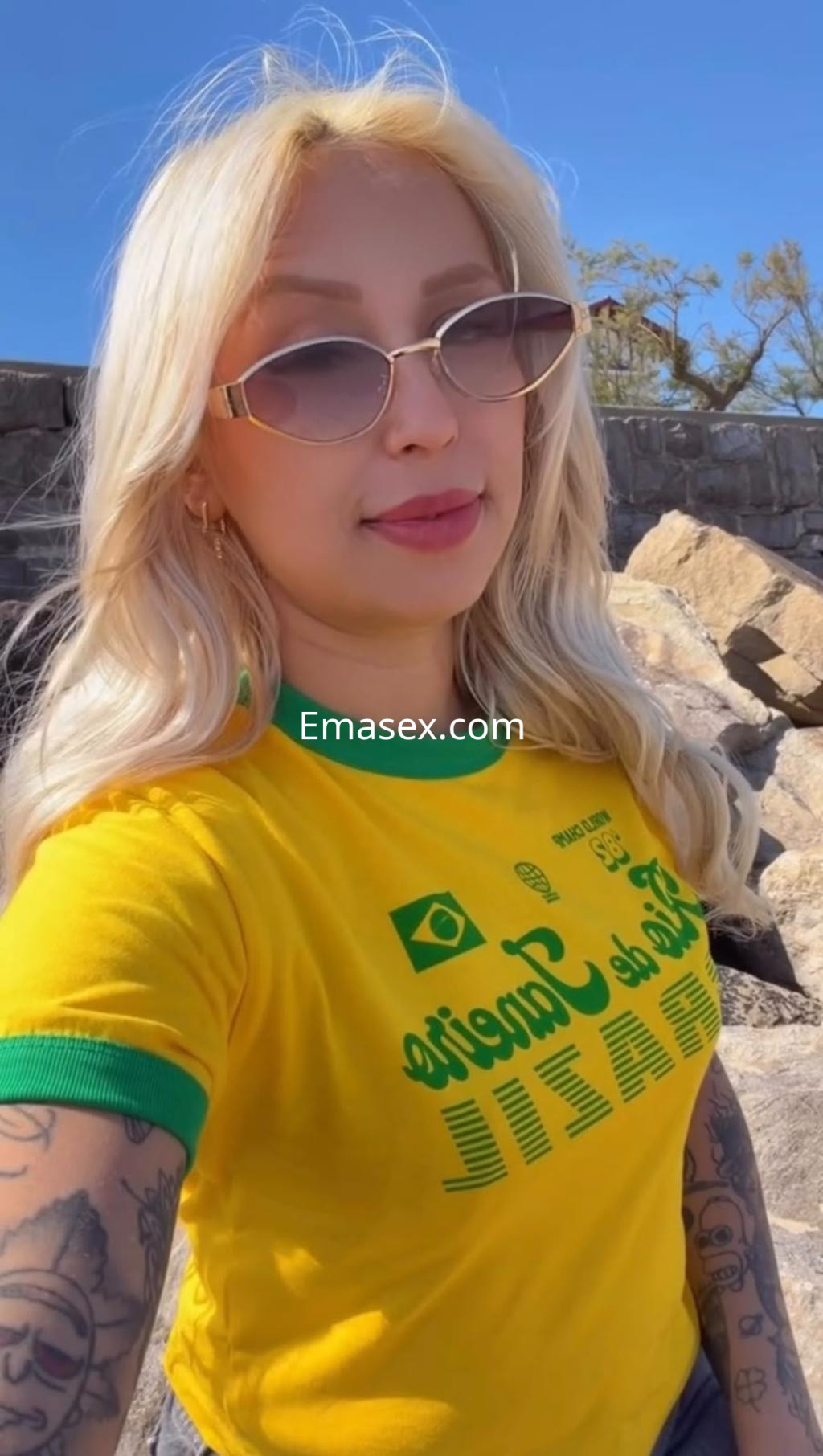 Escort en Vitoria, con cabello largo y rubio, viste una camiseta amarilla con detalles verdes, en un entorno natural.