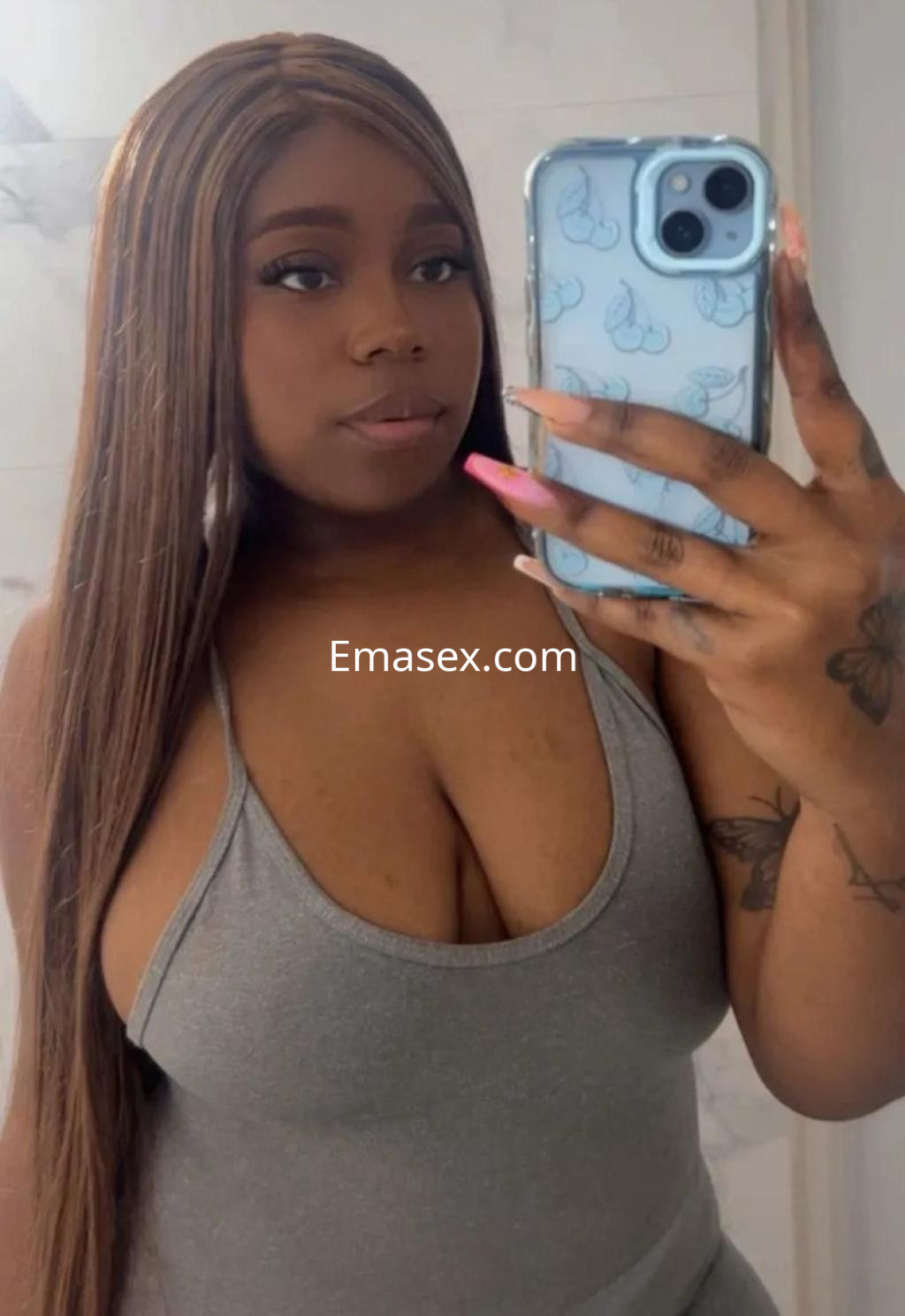 Escort en Granada, con cabello largo y lacio, viste un top gris que resalta su figura mientras toma un selfie.