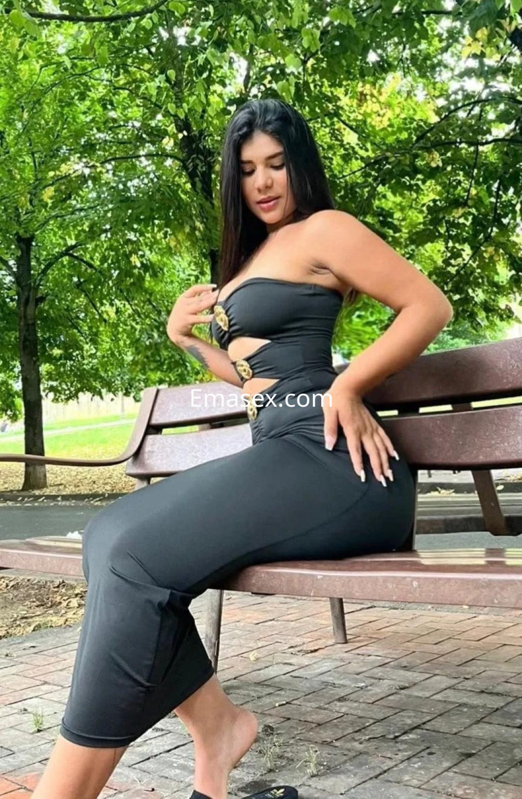La puta viste un ajustado vestido negro con detalles dorados, posando en un parque de Bilbao.