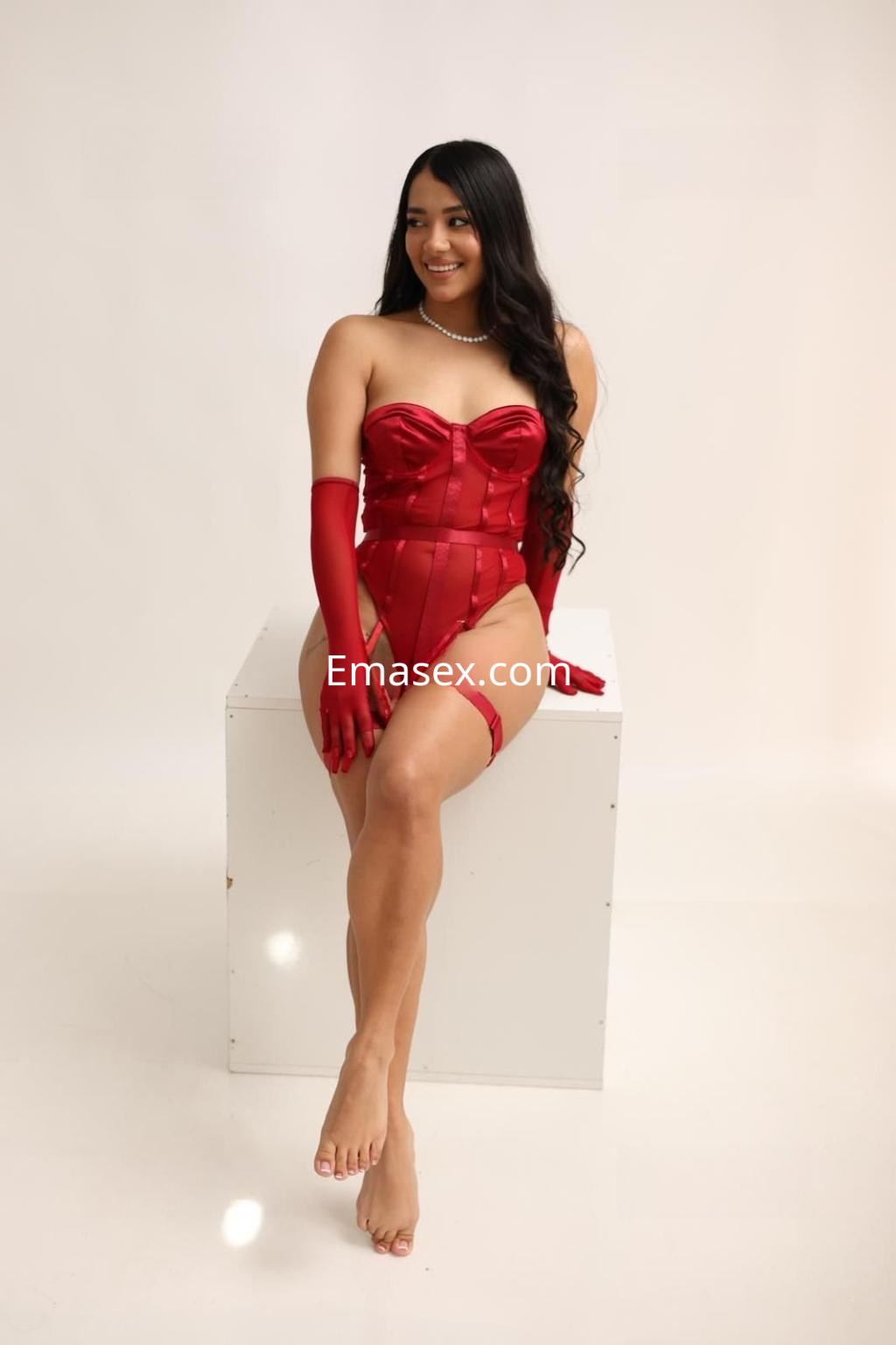 Escort en Albacete posando sobre un pedestal, vestida con un corset rojo, guantes largos y una sonrisa.