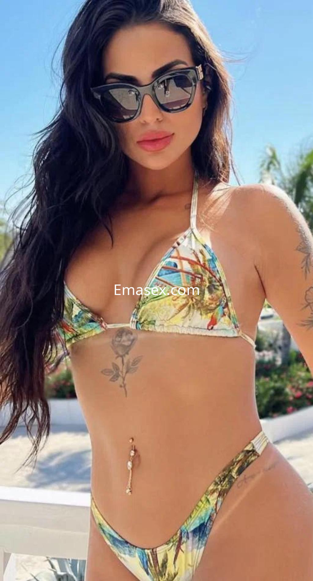 Escort en Alicante con cabello oscuro y rizado, vistiendo un bikini con estampado colorido y gafas de sol.