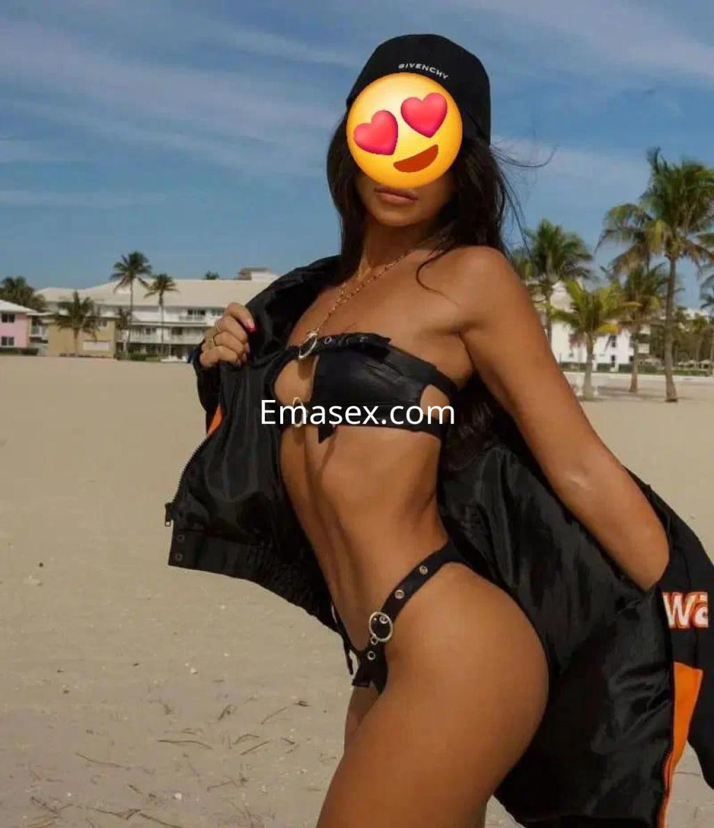 Escort en Alicante posando en la playa con un bikini negro y una chaqueta, mostrando su figura estilizada.