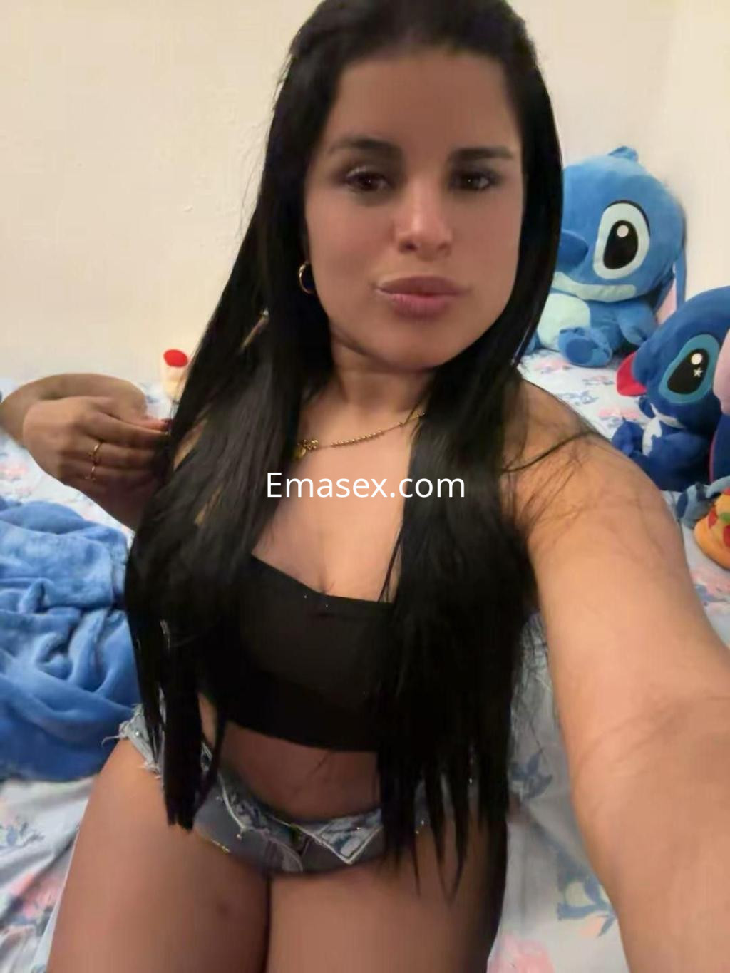 Escort en Córdoba con cabello largo y oscuro, vistiendo una blusa negra y shorts, posando en un entorno acogedor.