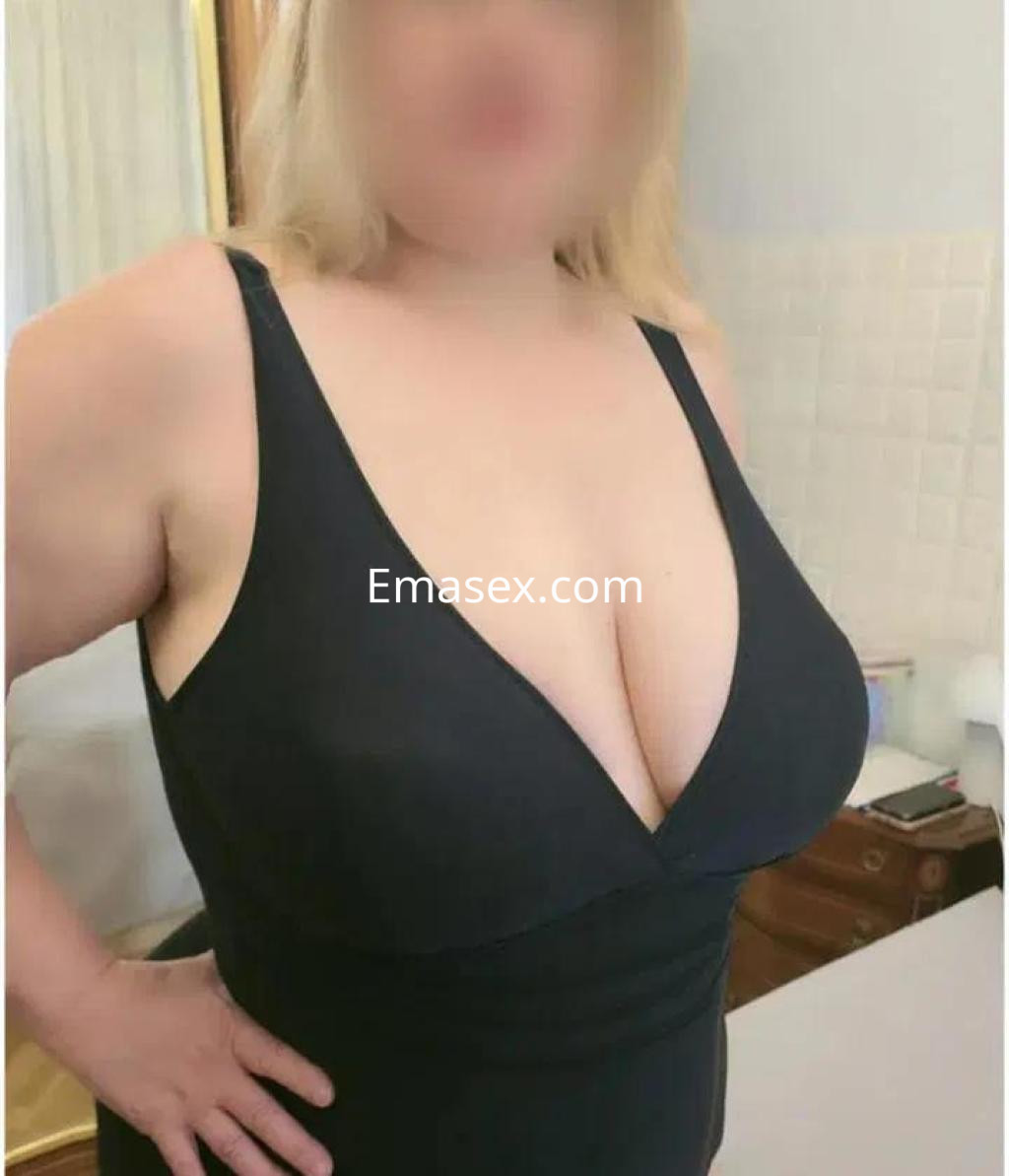 Puta con cabello rubio, viste un vestido negro con escote y posa en un entorno interior en Lleida.