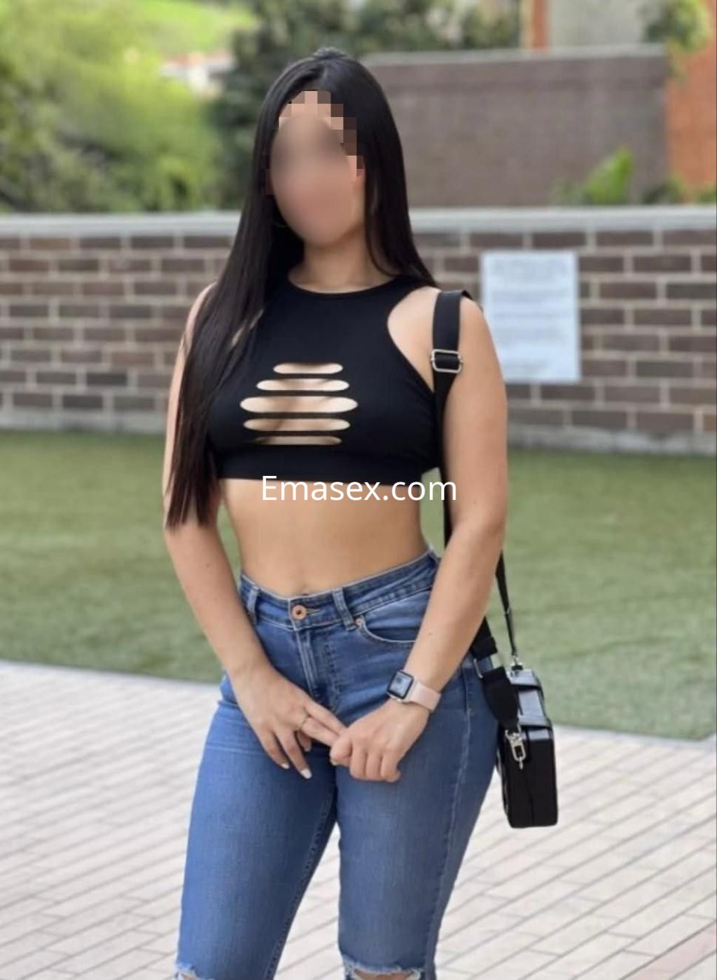Escort en Lugo con top negro de cortes, jeans ajustados y bolso cruzado, posando en un entorno al aire libre.