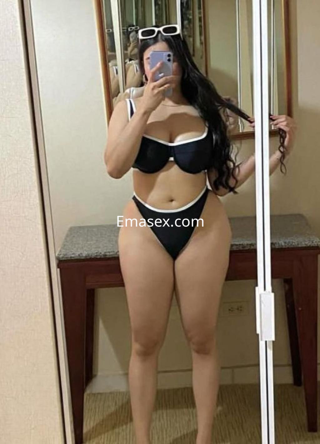 La puta lleva un bikini negro con detalles en blanco, posando frente a un espejo en un ambiente interior de Salamanca.