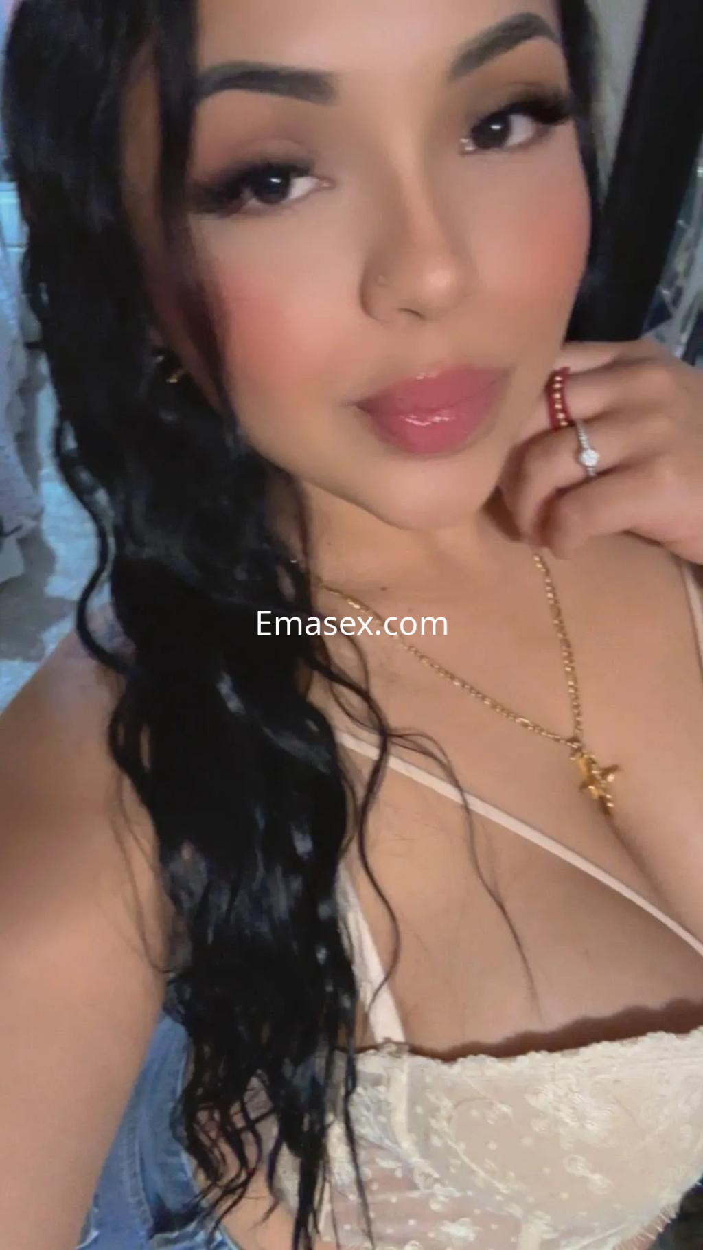 Escort en Sevilla con cabello largo y ondulado, luciendo un top claro y una cadena dorada, sonriente.