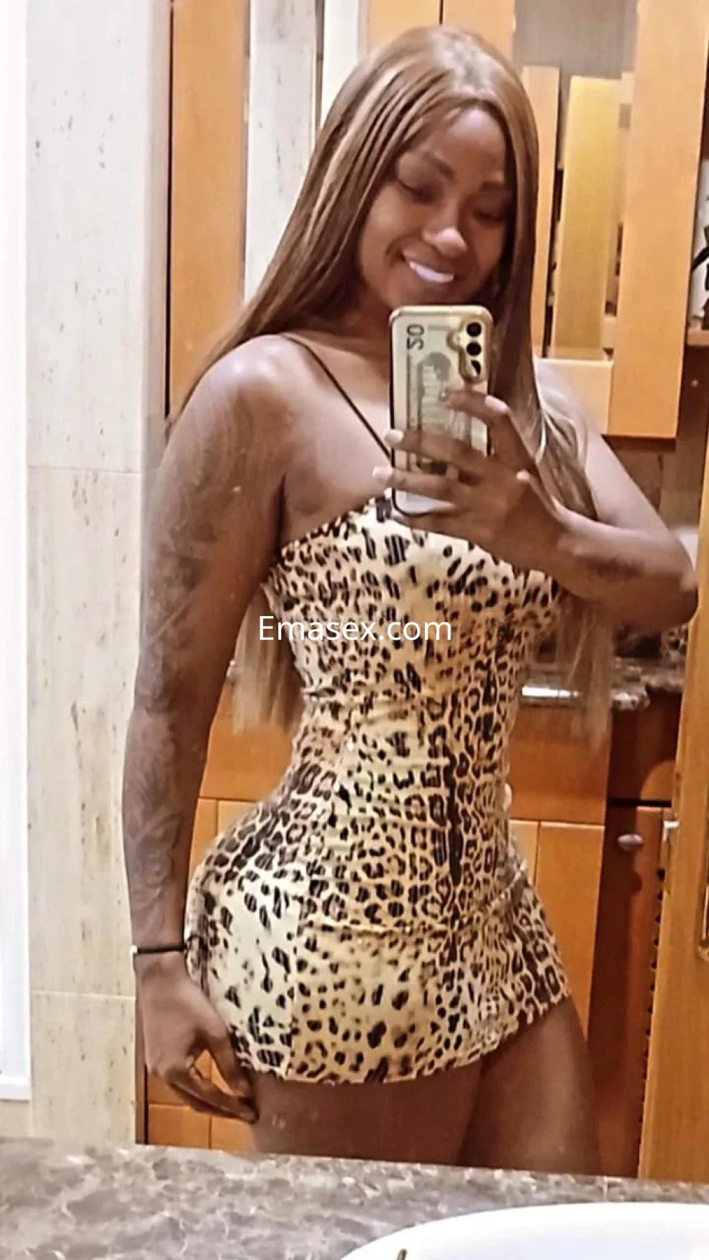 La puta posa sonriente frente al espejo, luciendo un vestido corto de leopardo en un baño de Valencia.