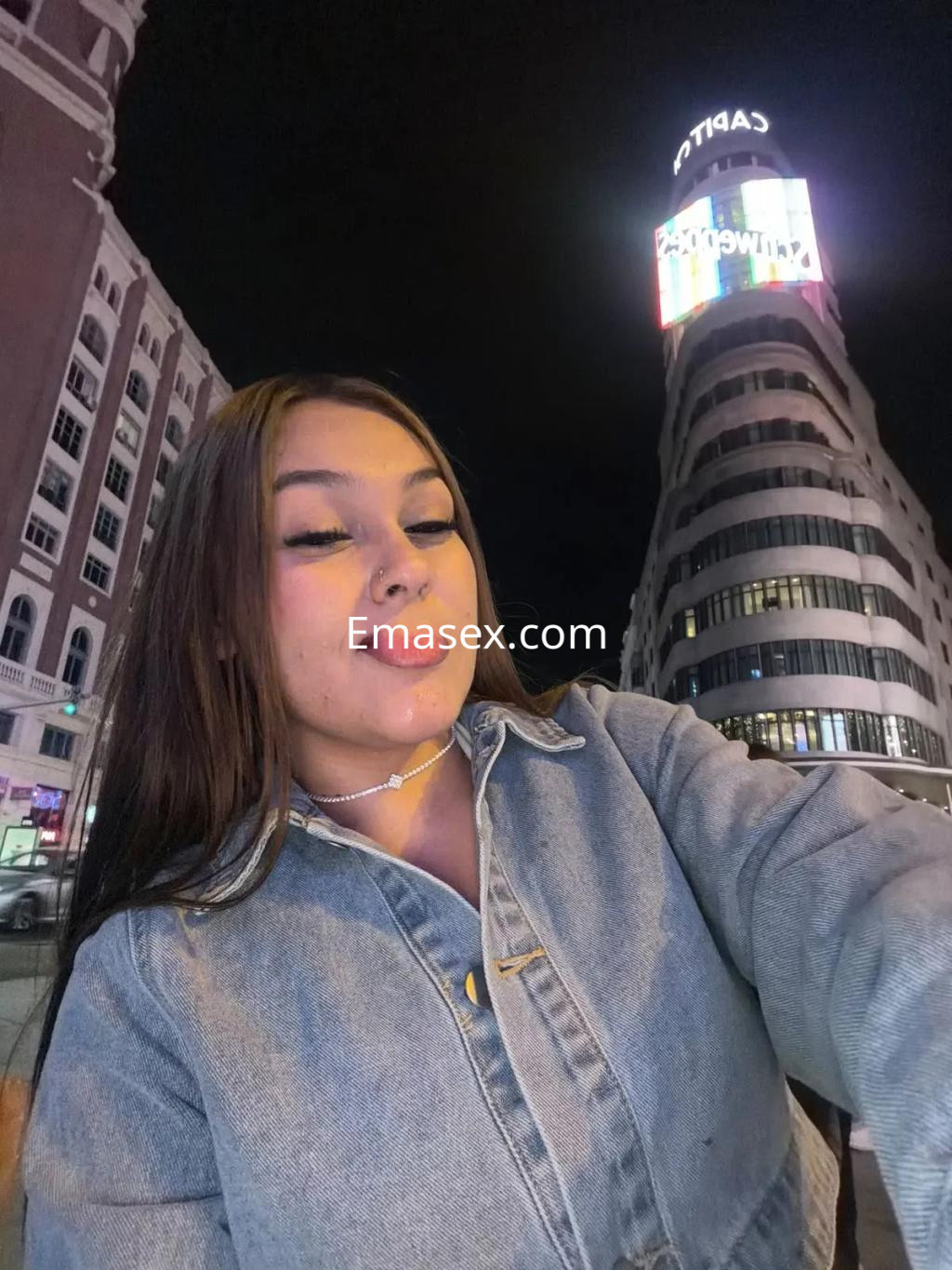 Escort en Zaragoza con cabello largo y lacio, vistiendo chaqueta de mezclilla, posando en un entorno urbano nocturno.