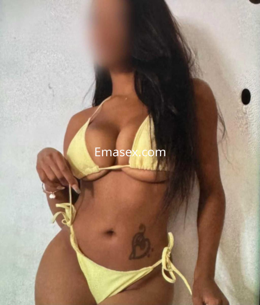 Escort en Zaragoza con cabello largo y oscuro, luciendo un bikini amarillo y mostrando un tatuaje en el abdomen.