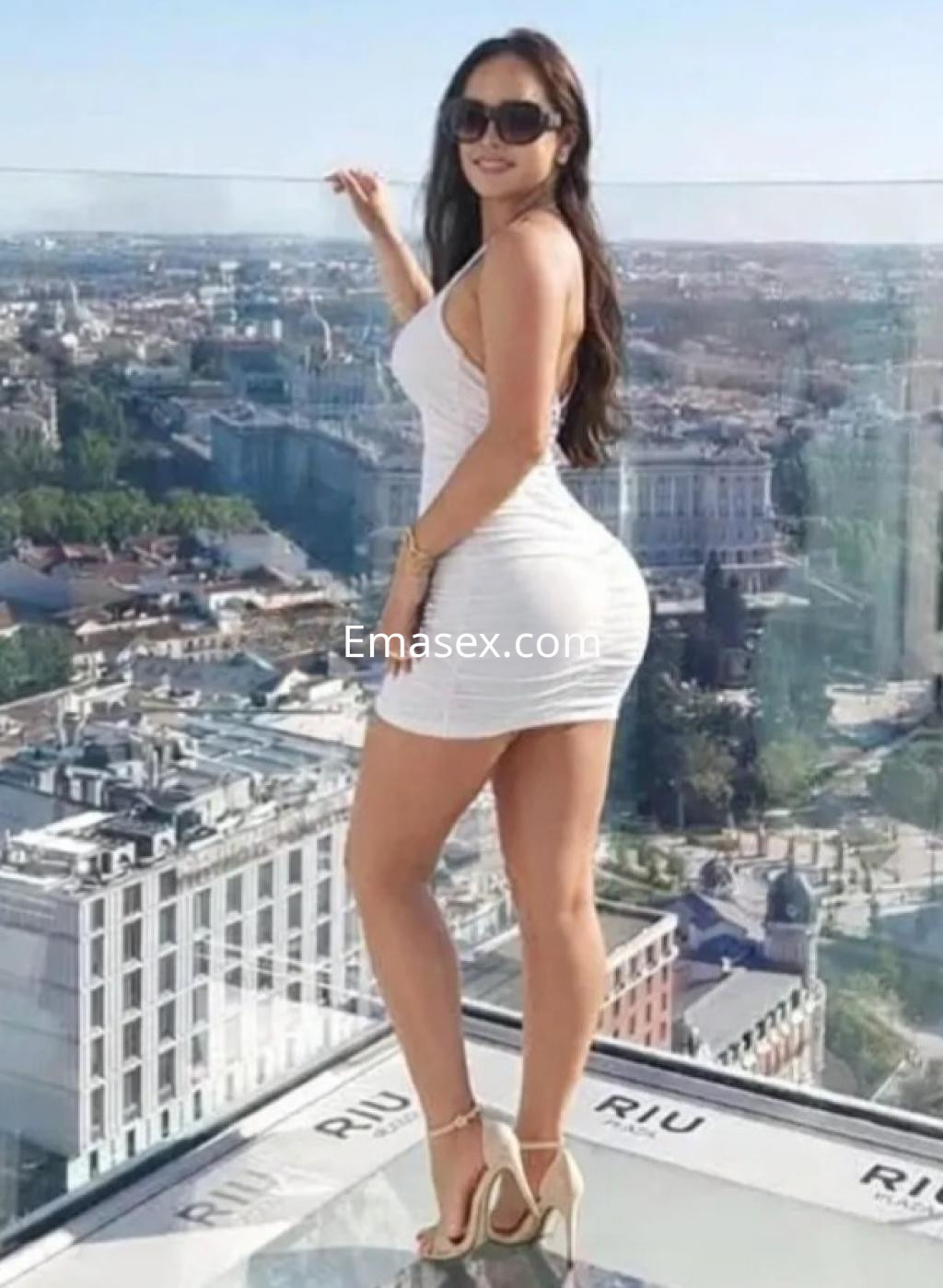 La puta posa con un vestido blanco ajustado y sandalias altas, con la ciudad de Málaga de fondo.