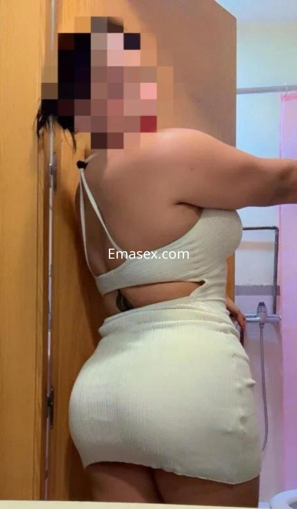 Escort en Castellón posando de perfil con un vestido blanco ajustado que destaca su figura y cabello recogido.