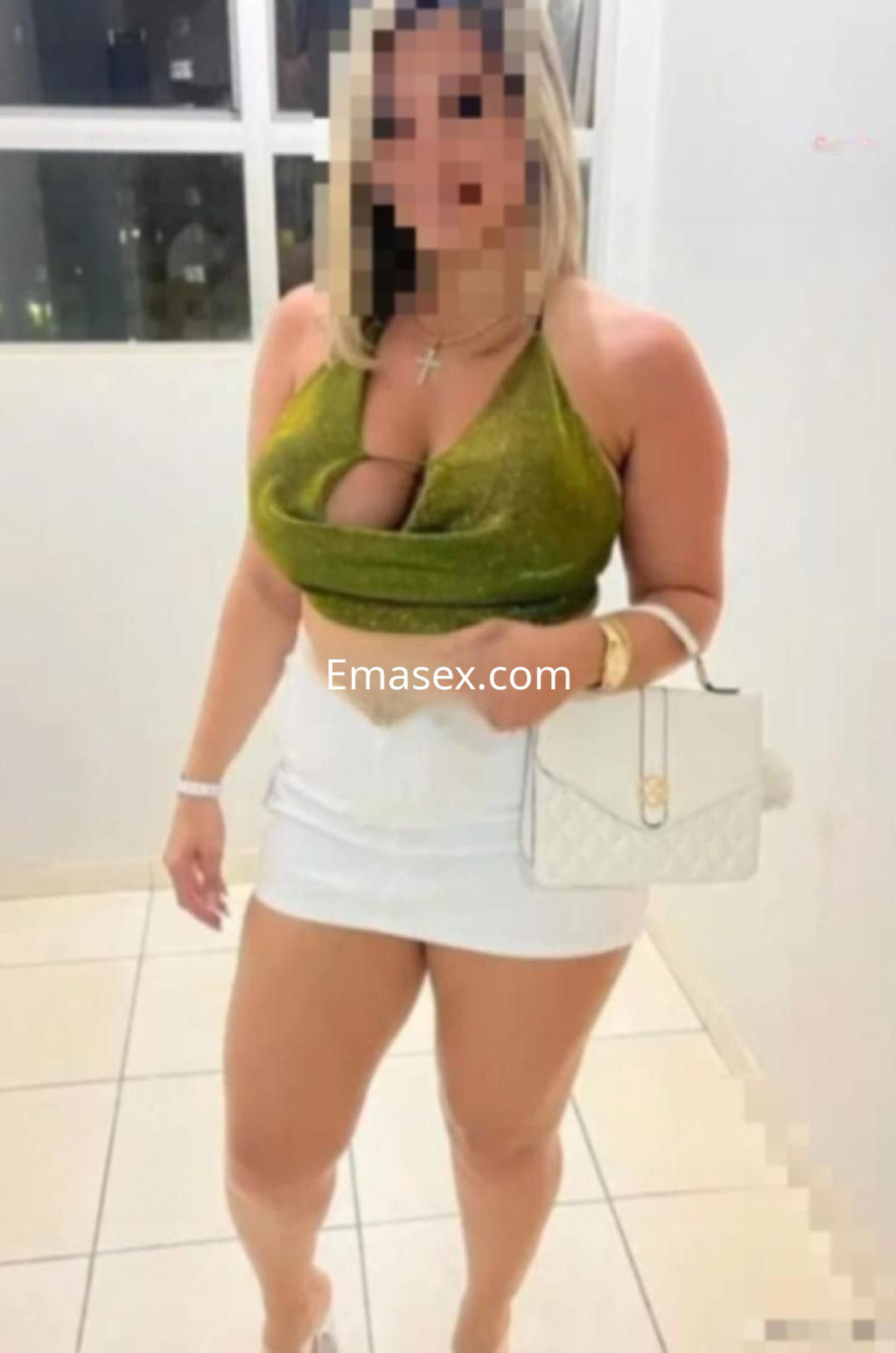 Puta en Pamplona con blusa verde brillante y falda blanca ajustada, posando en un entorno interior.