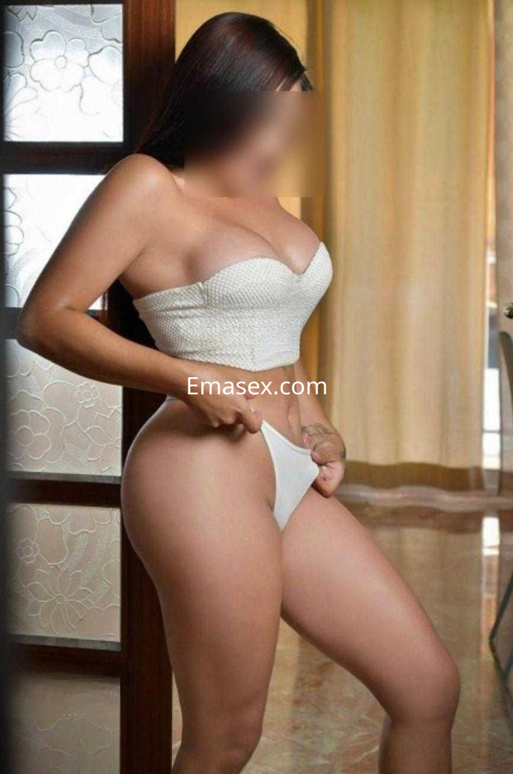 Escort en Salamanca, de pie en una habitación, viste un top blanco y una parte inferior del mismo color, con cabello largo.